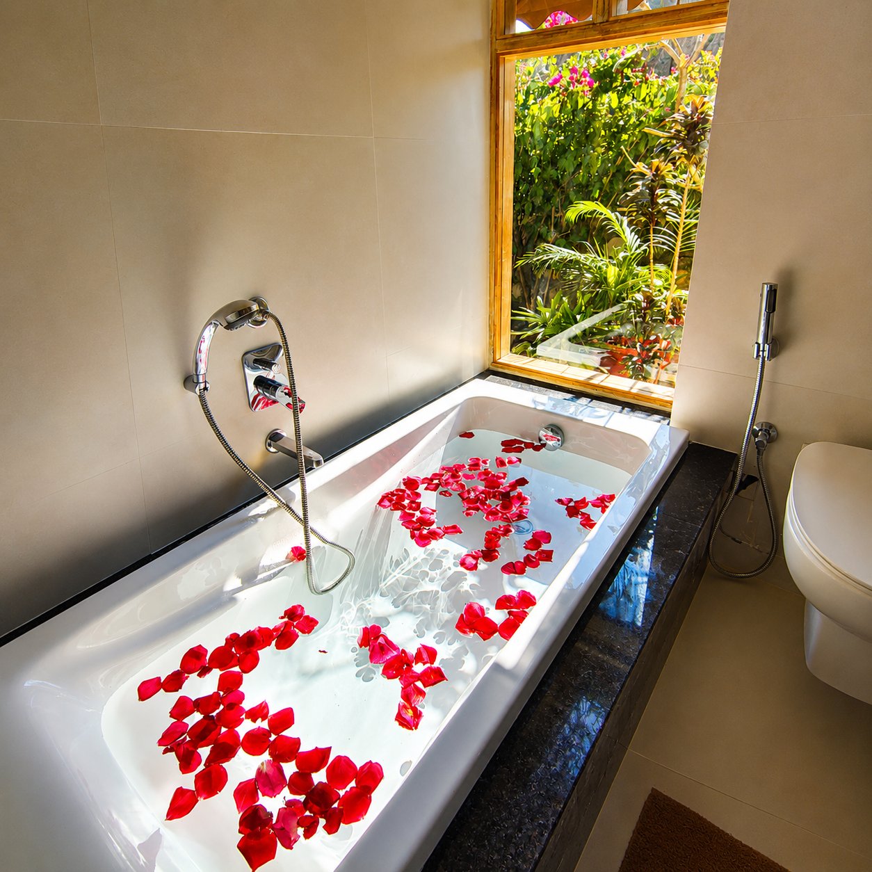 A bathtub decorated with rose petals beside a garden window
